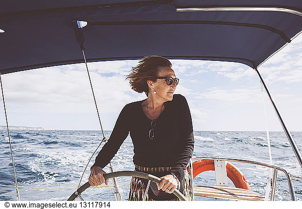 Mature woman driving boat on sea against sky