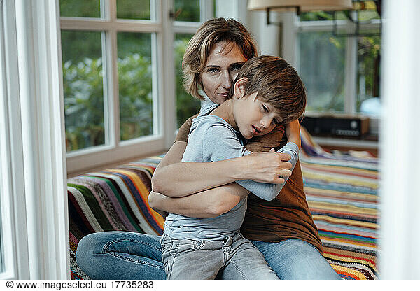 Mature woman embracing son sitting on sofa at home