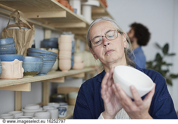 Mature woman examining bowl in art class