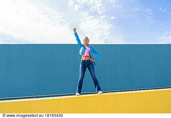 Mature woman gesturing fist standing on wall