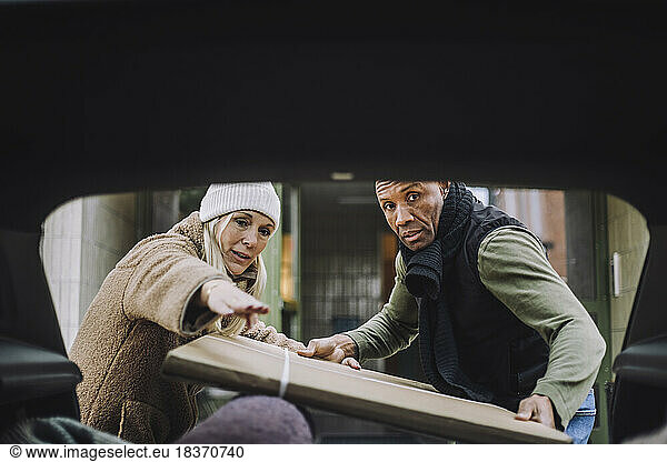 Mature woman guiding man loading cardboard in car trunk