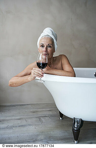 Mature woman having red wine in bathroom