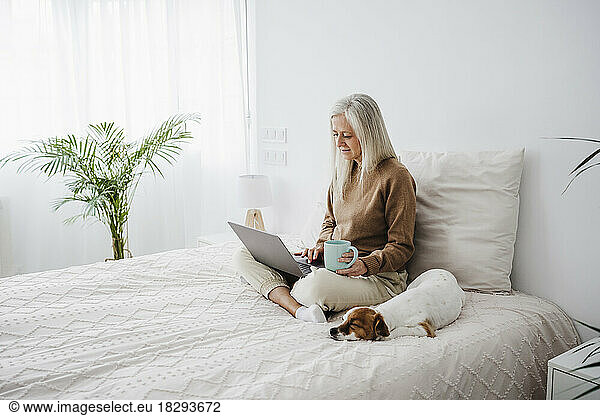 Mature woman holding coffee cup and using laptop at home