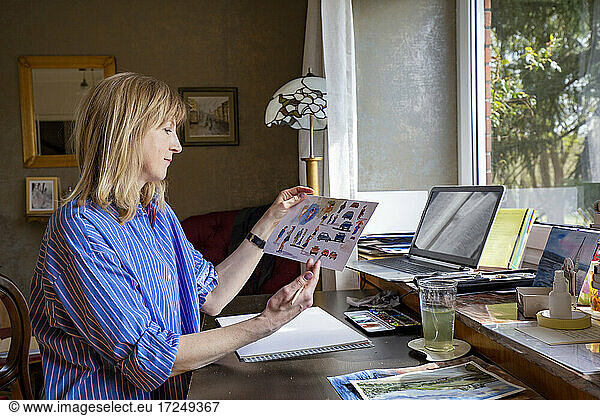 Mature woman holding colored sketch on table at home