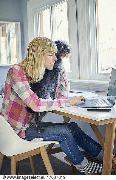 Mature woman holding dog and working from home