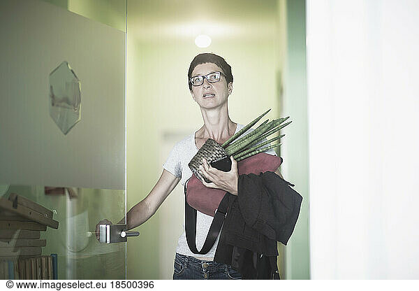 Mature woman holding houseplant and open the door in the office  Freiburg im Breisgau  Baden-Württemberg  Germany