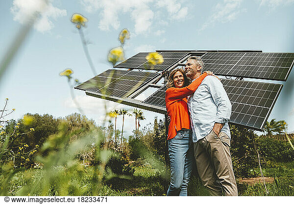 Mature woman hugging man standing in front of solar panels