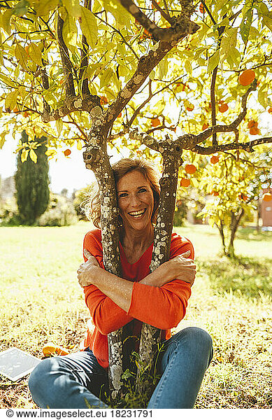 Mature woman hugging orange tree on sunny day