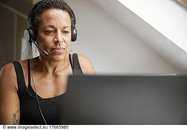 Mature woman in headset working from home at laptop