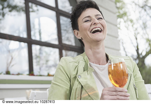 Mature woman laughing with aperol spritzat at sidewalk cafe  Bavaria  Germany