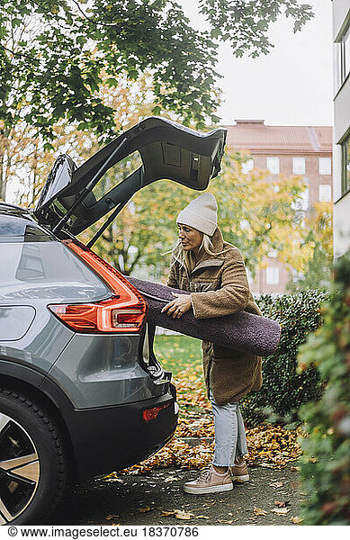 Mature woman loading carpet in car trunk