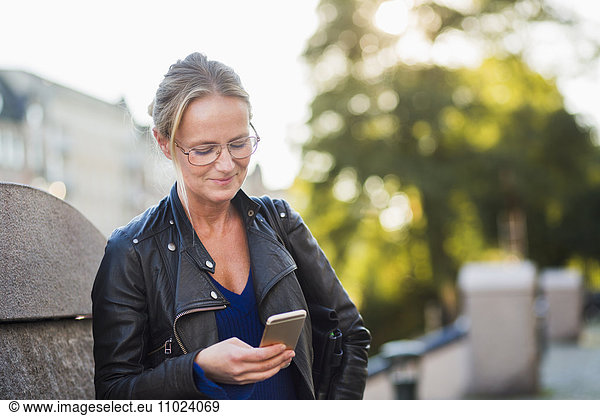 Mature woman looking at smart phone and smiling at street