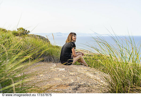 Mature woman looking away while sitting on cliff