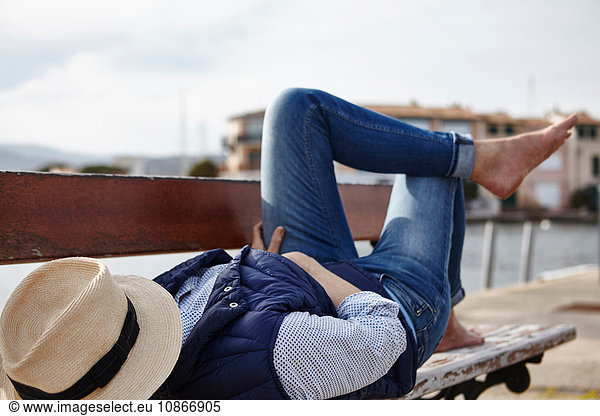 Mature woman lying on bench  hat covering face