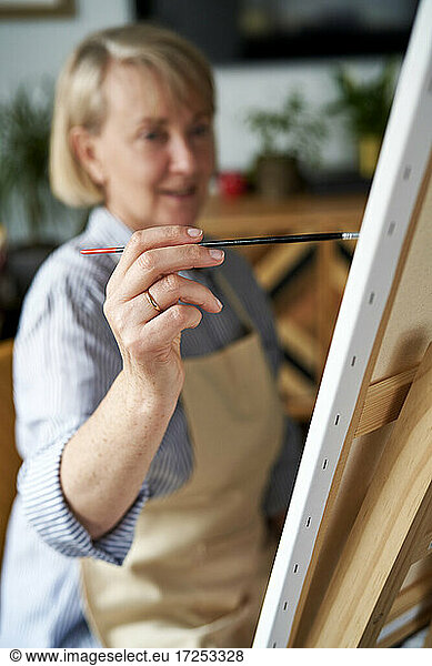 Mature woman making painting on easel at home
