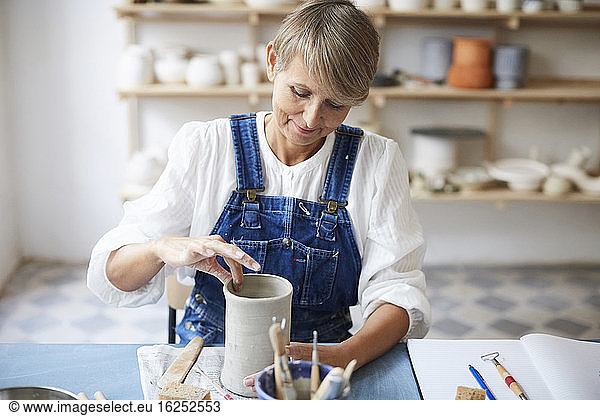 Mature woman molding earthenware at table in art class