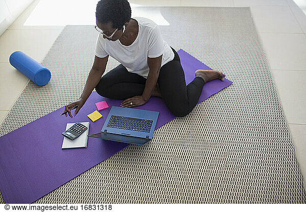 Mature woman paying bills and working at laptop on yoga mat