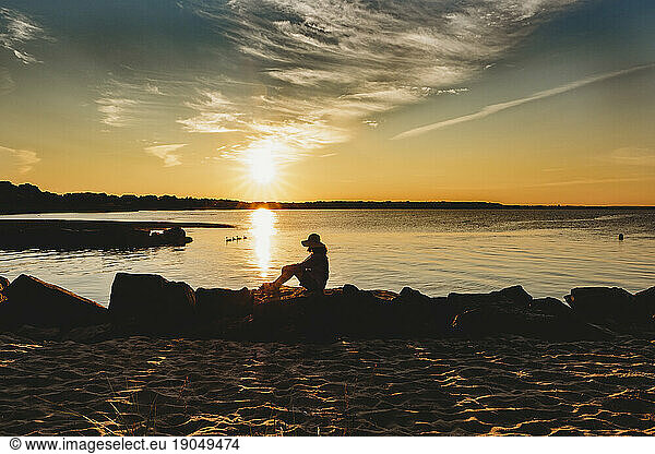 Mature woman peacefully sitting on Cape Cod beach in the golden hour