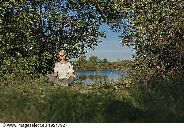 Mature woman practicing lotus position and meditating at lakeshore