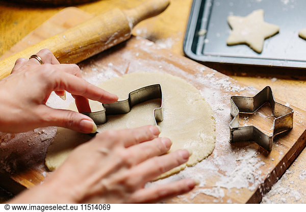 Mature woman pressing cookie cutter into dough  close-up