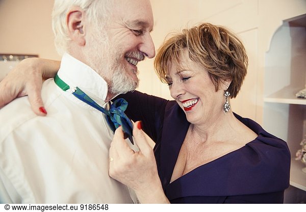 Mature woman putting bow tie on senior man