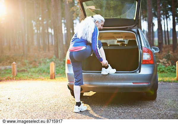 Mature woman putting on trainers on car boot
