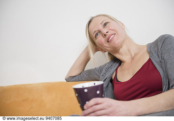 Mature woman relaxing on couch with cup  smiling