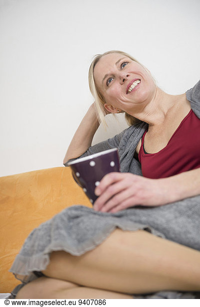 Mature woman relaxing on couch with cup  smiling