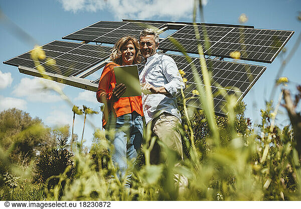 Mature woman sharing tablet PC with man in front of solar panels