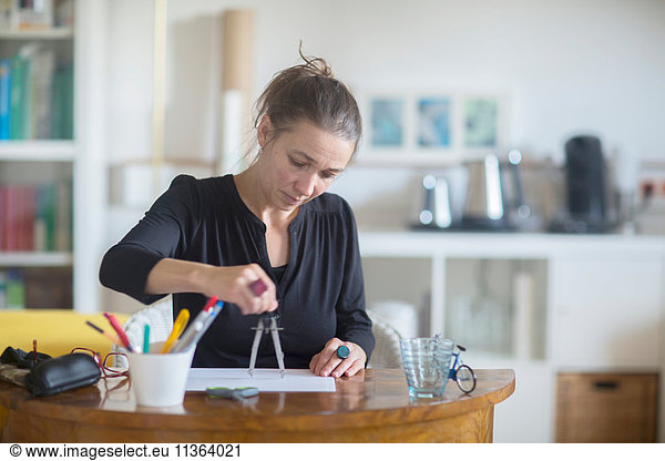 Mature woman sitting at desk  using pair of compasses