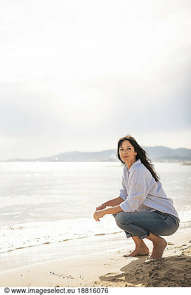 Mature woman spending leisure time crouching on sand at beach