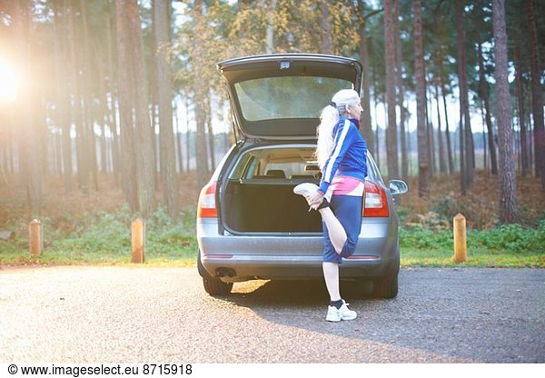 Mature woman stretching leg by car