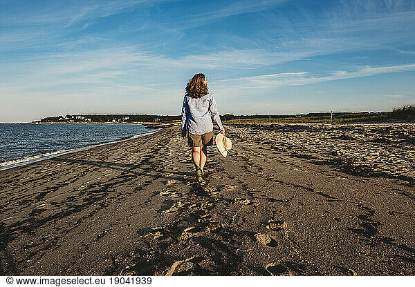 Mature woman strolling on Cape Cod beach with hat in hand