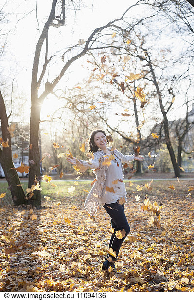 Mature woman throwing autumn dry leaves in air in the park  Bavaria  Germany