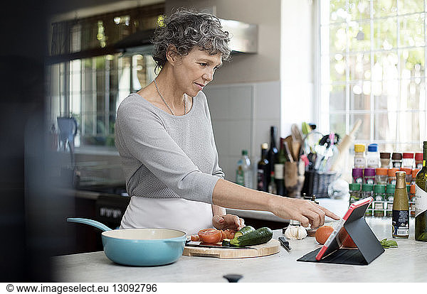 Mature woman using digital tablet while cooking in kitchen