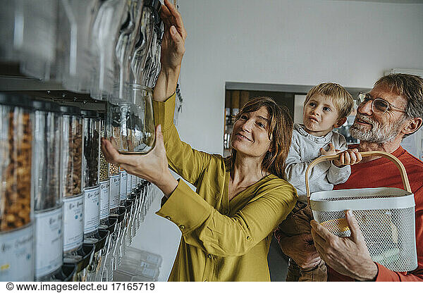 Mature woman using food dispenser while father carrying son at zero waste shop