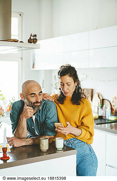 Mature woman using mobile phone by man in kitchen at home