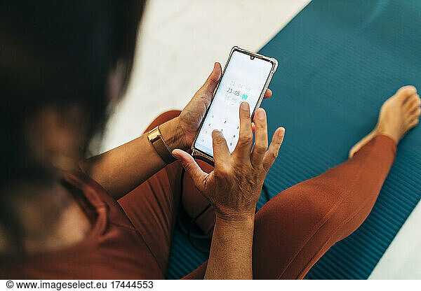 Mature woman using mobile phone while sitting on exercise mat at home