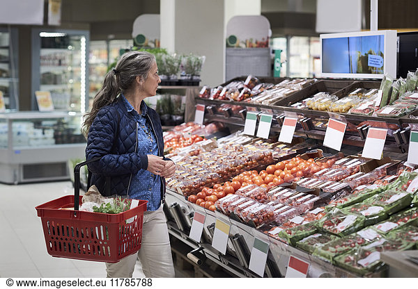 Mature woman walking by vegetables rack at supermarket