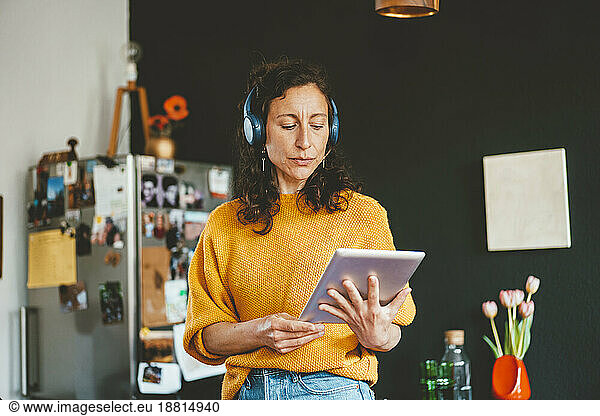 Mature woman watching tablet PC wearing wireless headphones at home