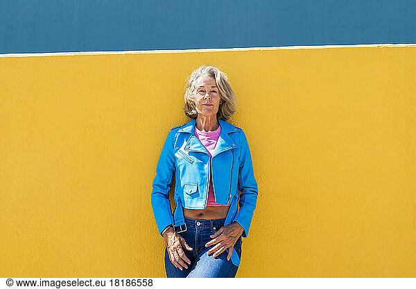 Mature woman wearing blue leather jacket in front of wall