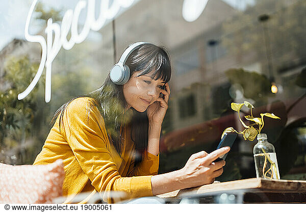 Mature woman wearing wireless headphones using smart phone in cafe