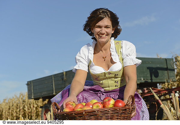 Mature woman with basket full of apples in field  smiling