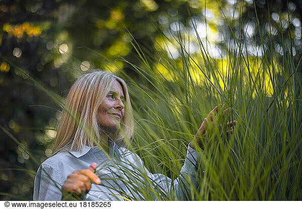 Mature woman with blond hair touching plant in garden