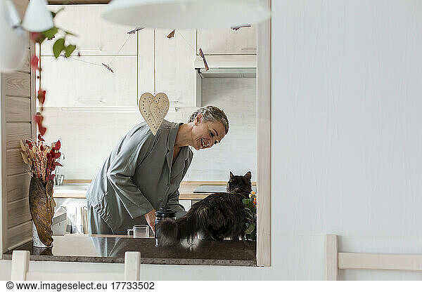 Mature woman with cat in kitchen at home