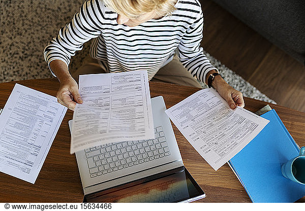 Mature woman with documents using laptop at home
