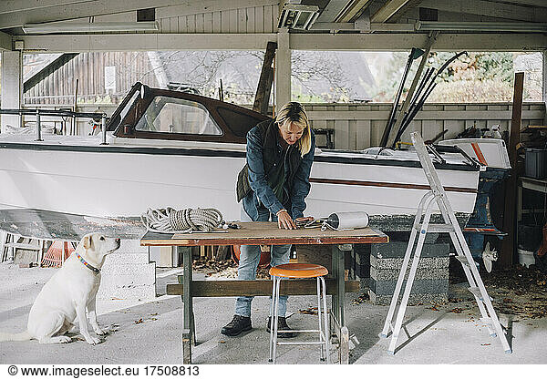 Mature woman with dog repairing nautical vessel in garage