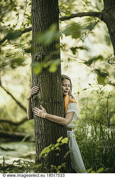 Mature woman with eyes closed embracing tree in forest