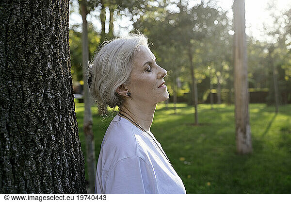 Mature woman with eyes closed standing near tree in park