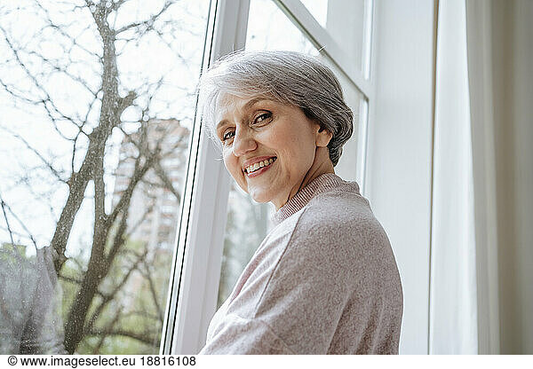 Mature woman with gray hair near window at home